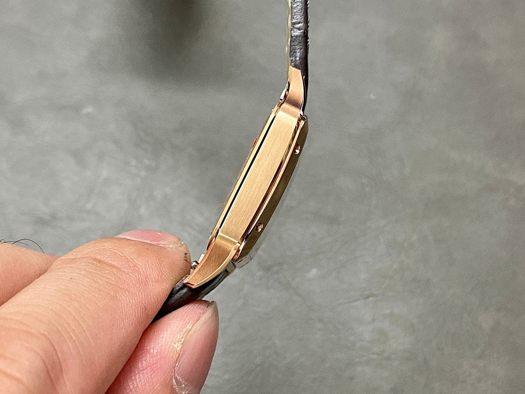 Cartier wristwatch side view: rose gold case edges and crown, black leather strap on hand
