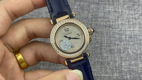 Gold Cartier watch with diamond ring bezel, light dial, blue leather band, date subdial.
