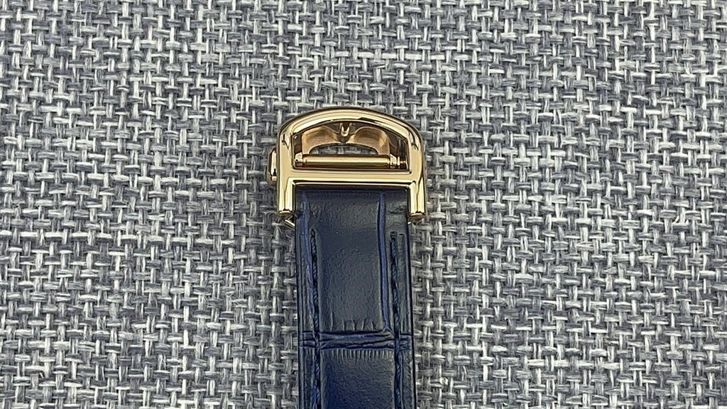 Gold Cartier watch case with blue leather strap, top buckle clasp view.