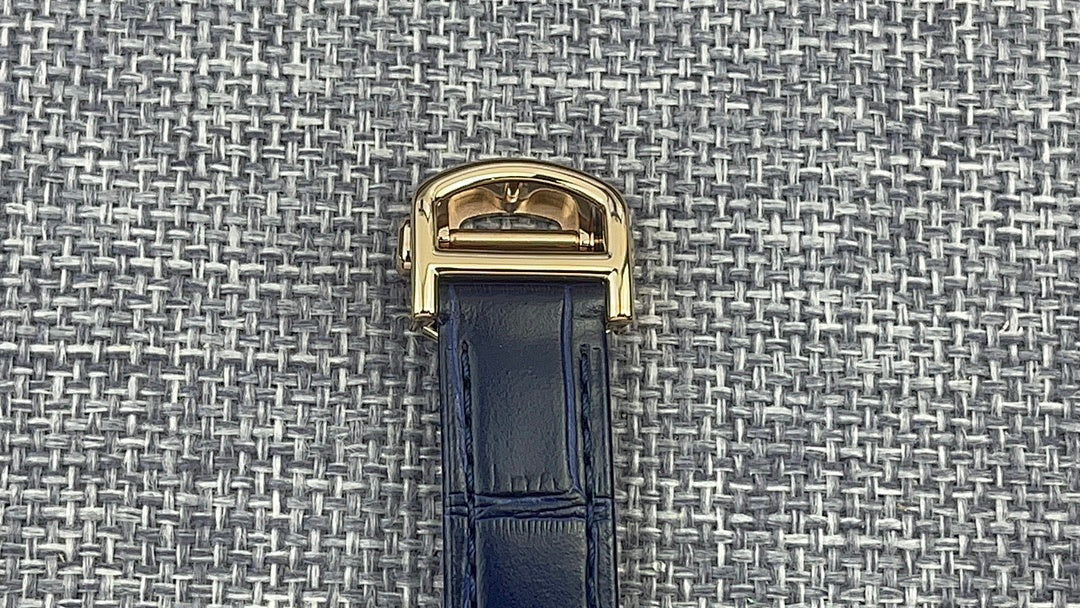 Gold Cartier watch case with blue leather strap, top buckle clasp view.