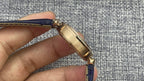 Gold Cartier watch side profile with blue leather strap and gold crown detail.