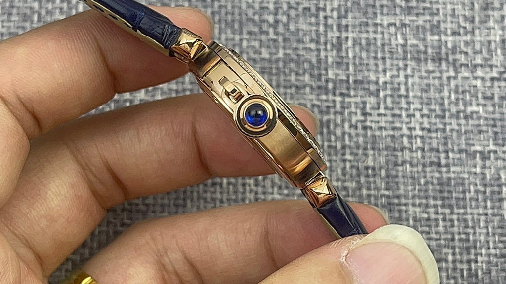 Gold Cartier watch side with blue leather strap, gold bezel and sapphire crown.
