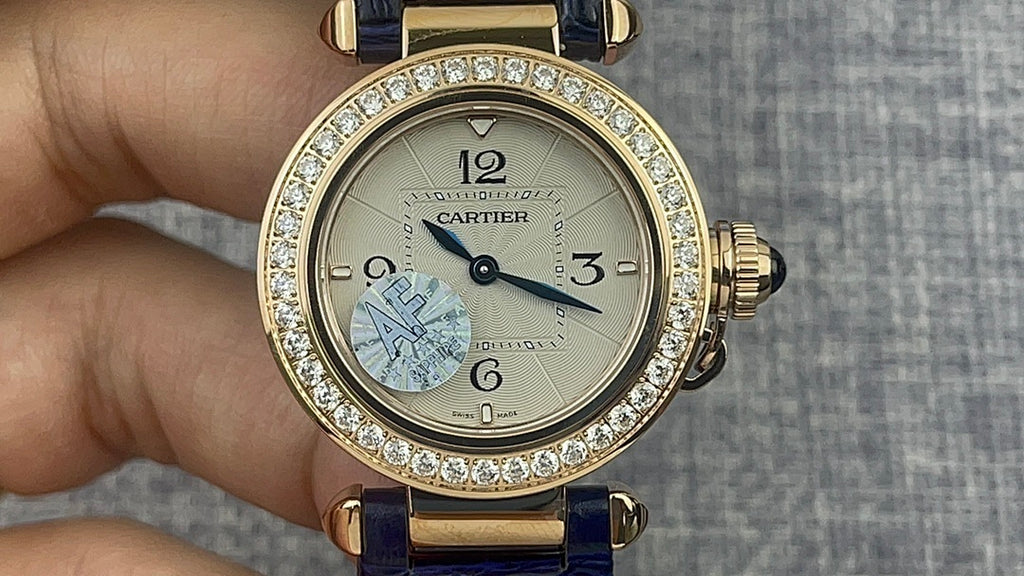 Gold Cartier wristwatch with diamond bezel, white dial, Arabic numerals, blue leather strap.