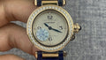 Gold Cartier wristwatch with diamond bezel, white dial, Arabic numerals, blue leather strap.