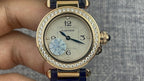 Gold Cartier wristwatch with diamond bezel, white dial, Arabic numerals, blue leather strap.