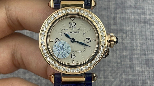 Gold Cartier wristwatch with diamond bezel, white dial, Arabic numerals, blue leather strap.