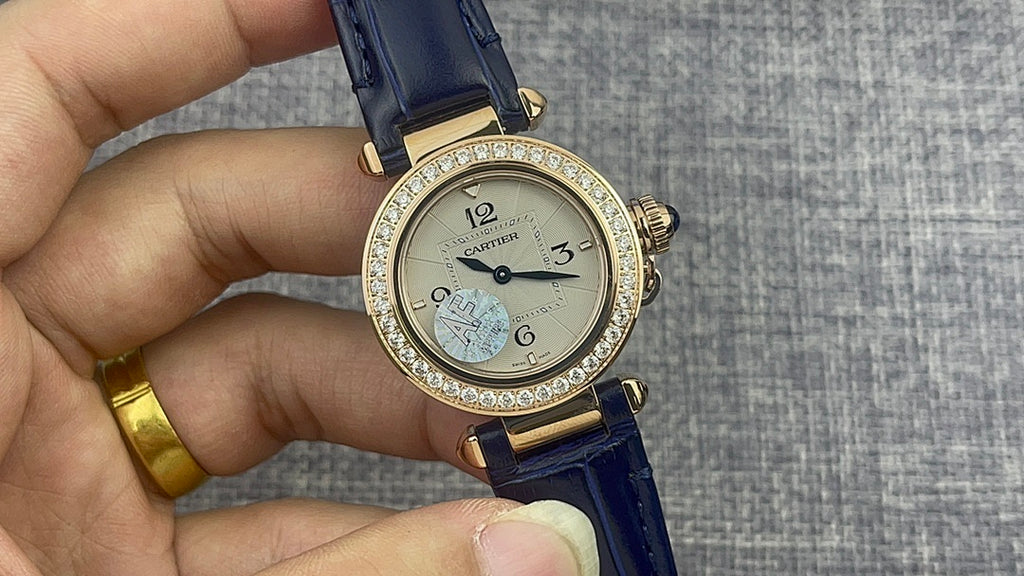 Gold Cartier watch front with diamond bezel, white dial, black hands, blue leather strap.