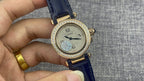 Gold Cartier watch front with diamond bezel, white dial, black hands, blue leather strap.