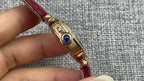 Cartier wristwatch with gold case and blue detail on the side, red leather strap