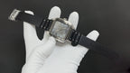 Cartier wristwatch on black leather strap with silver case and Roman numeral dial.