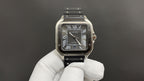 Cartier wristwatch with Roman-numeral black dial, silver case, and black leather strap.