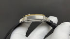 Gold-tone and silver-toned watch case with black leather strap, side profile