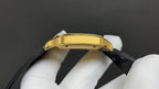 Gold watch case top view with black strap, crown and bezel screws visible