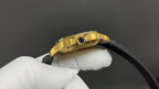 Gold Cartier watch side view with crown and blue gem, black strap attached