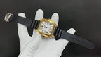 Gold watch on black leather strap, rectangular bezel, white dial with Roman numerals