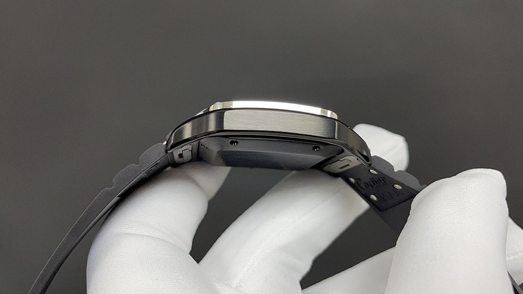 Cartier watch underside with black strap and metal case, held by white gloves.