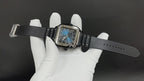 Cartier watch on wrist with black strap, blue dial visible in white gloves.