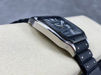Cartier wristwatch side view with steel case edge and black bracelet links on a tan support.