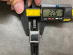 Cartier wristwatch with black leather strap, silver case, held in a caliper measuring tool