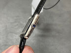 Cartier watch side profile with silver case, crown with blue gem, and black leather strap