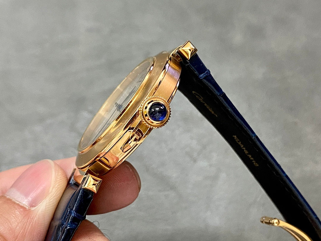 Cartier watch with gold-tone round case and blue leather strap, gemstone crown detail