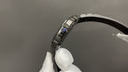 Cartier watch side profile with crown and black leather strap, silver-toned case edge visible.