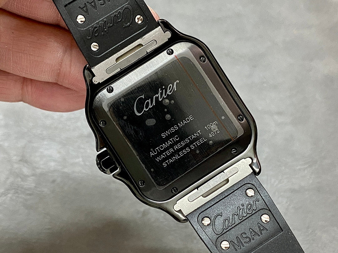 Cartier watch case back with engraved markings and black strap with metal pins.