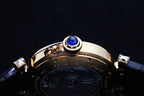 Cartier watch crown with blue gem on gold-tone bezel above dark leather strap