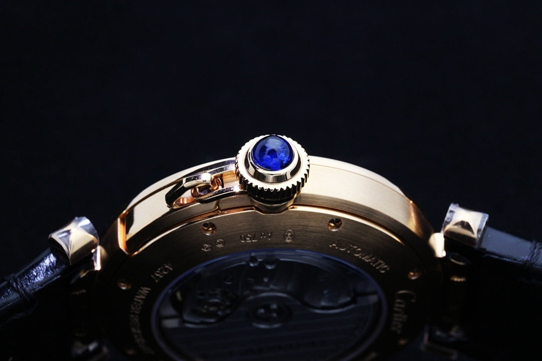 Cartier watch crown with blue gem on gold-tone bezel above dark leather strap