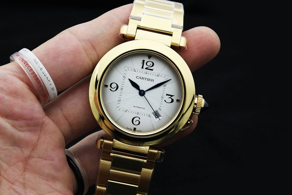 Cartier gold-tone watch held in hand, showing white dial and blue hands.