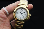 Cartier gold-tone watch held in hand, showing white dial and blue hands.