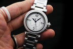 Cartier wristwatch on silver steel bracelet with diamond bezel and white dial, held in hand.