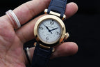 Cartier watch on wrist with blue leather strap, gold case, white dial and numerals