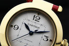Cartier watch dial close-up with gold bezel, white dial, blue hands, red leather strap