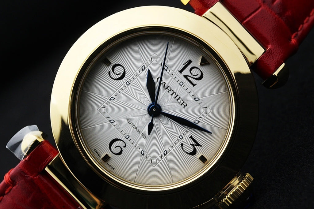 Cartier watch face with gold bezel, white dial, blue hands, red leather strap