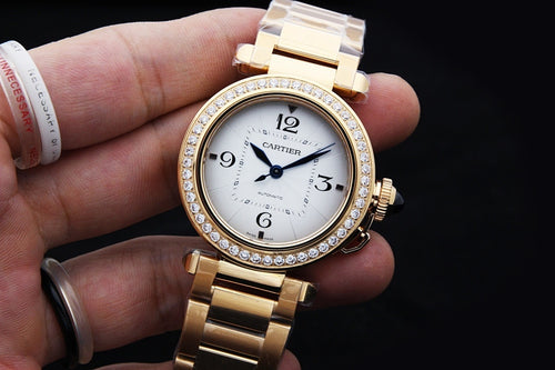 Gold wristwatch with diamond bezel, white dial, blue hands, and linked bracelet on hand