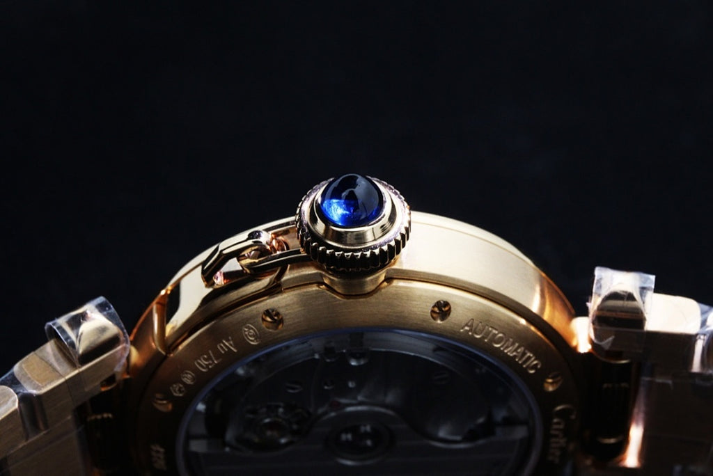 Gold wristwatch crown with blue gemstone and part of metal bracelet