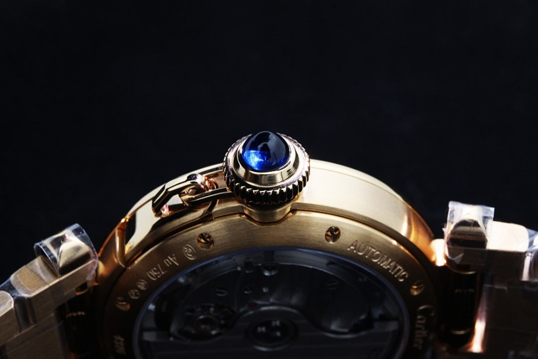 Gold wristwatch crown with blue gemstone and part of metal bracelet