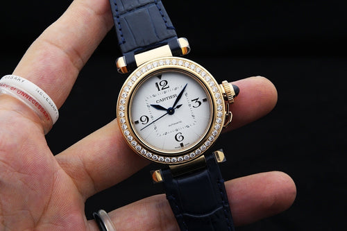 Gold-tone Cartier watch with white dial, diamond bezel, blue leather strap held in hand