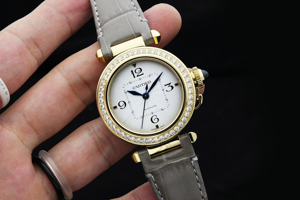 Cartier watch angled view with white dial, gold bezel with crystals, and gray strap