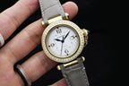Cartier watch angled view with white dial, gold bezel with crystals, and gray strap