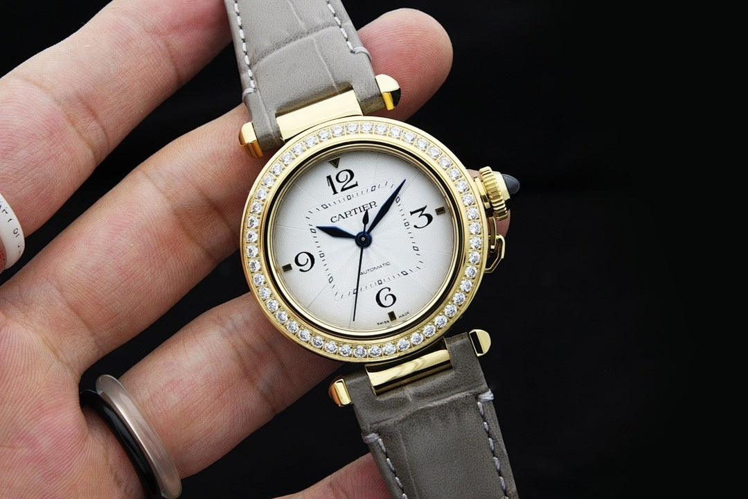 Cartier watch angled view with white dial, gold bezel with crystals, and gray strap