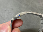 Cartier metal wristwatch with blue jewel on the side, silver bracelet visible.