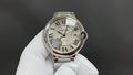 Cartier round steel watch with white dial, Roman numerals, blue hand and crown.