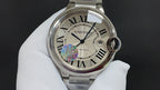 Cartier round watch with white dial, Roman numerals, blue center hand and date ring.