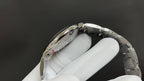 Wristwatch case back with metal bezel and bracelet links, angled view on white glove