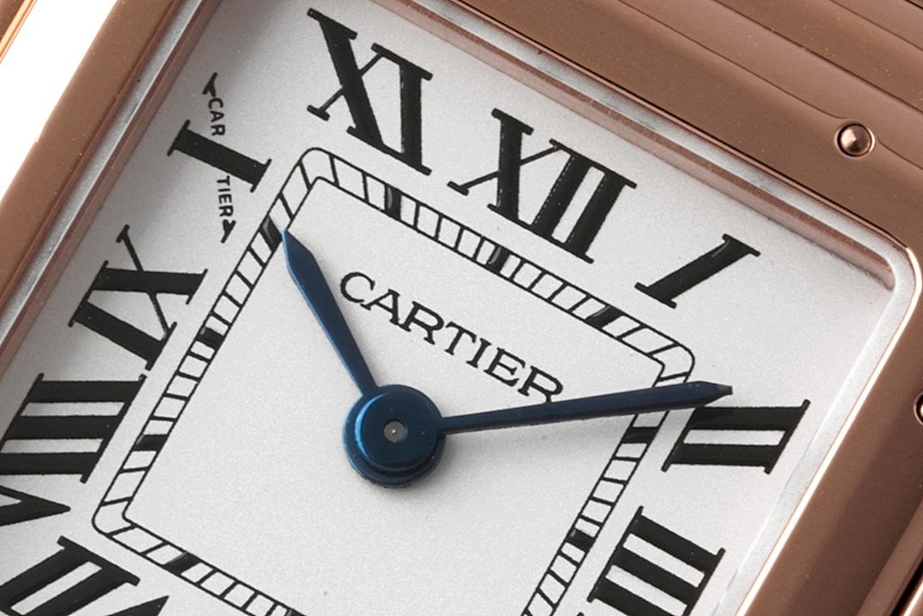Cartier watch dial close-up showing blue central hands and Roman numeral markers.