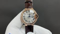 Cartier watch: white dial, Roman numerals, brown leather strap, rose gold case.