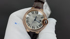 Cartier watch close-up: white dial with Roman numerals, brown leather strap, rose gold bezel.