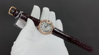 Cartier watch with brown leather strap and white dial, rose gold case, angled view.